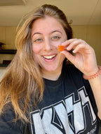 Person holding a small orange candy in front of their face, wearing a black shirt with white text.